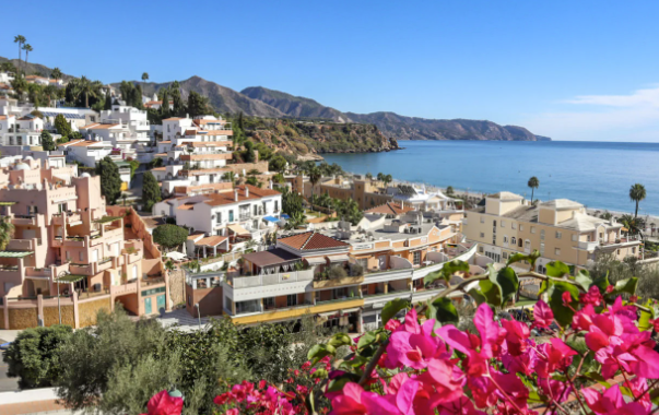 Bridge of Ronda, Spain, spanning a deep gorge with a waterfall, under a blue sky.