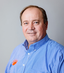 Man in blue shirt with orange logo smiles at the camera.