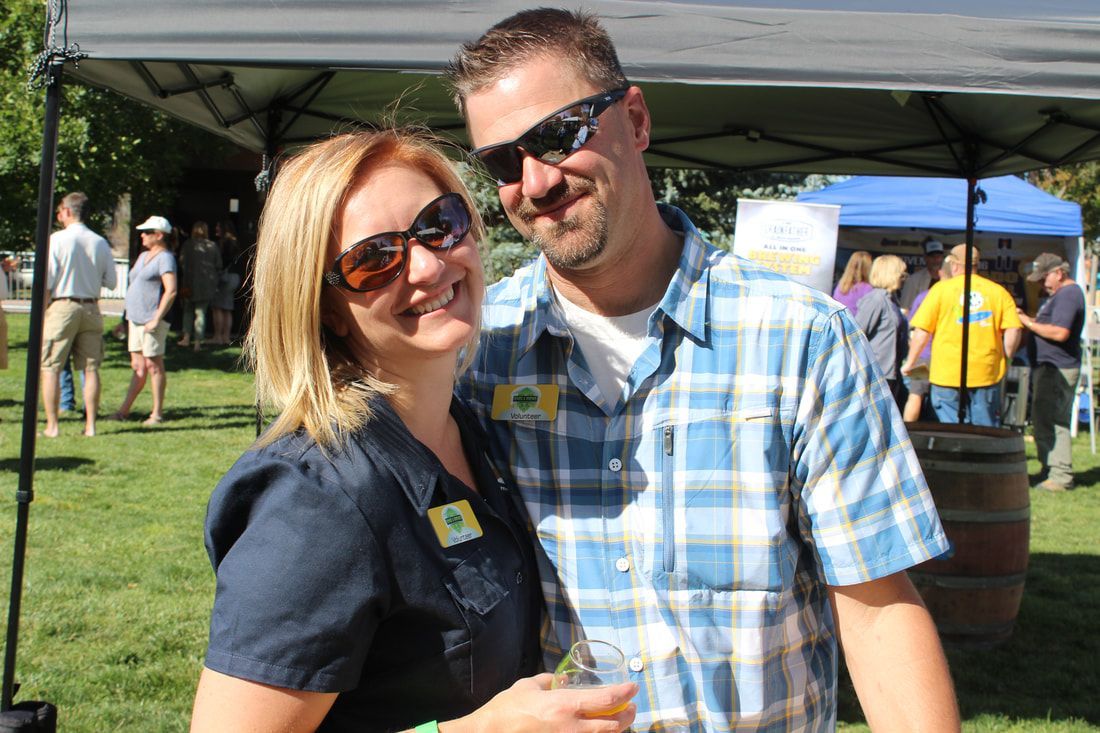 Couple smiling at an outdoor event, wearing sunglasses and casual clothing.