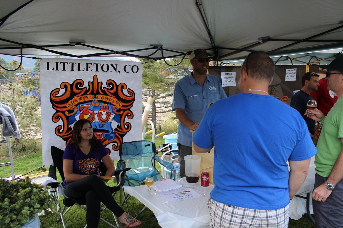 People at a Littleton, CO booth. Woman seated, others looking at a drinks/food setup.