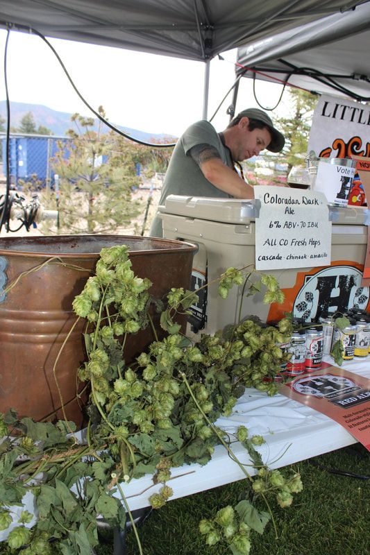 Man at a beer stand serving beer with fresh hops. Mountains in the background.