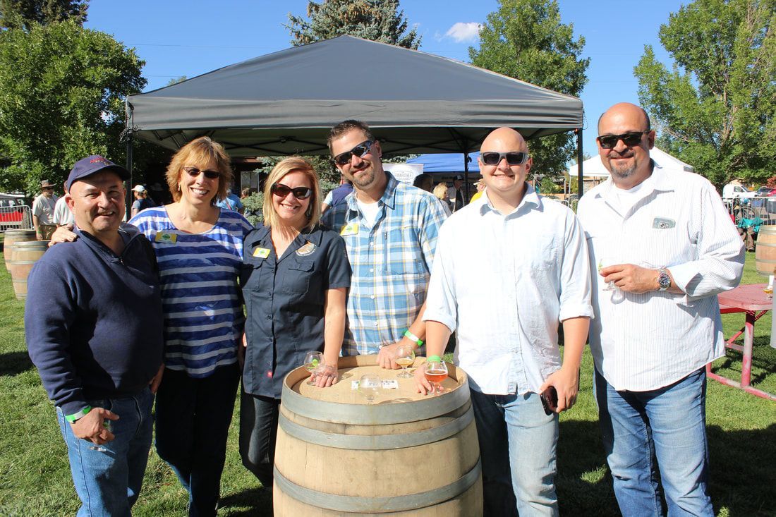 Group of people around a barrel outdoors, smiling, under a canopy.