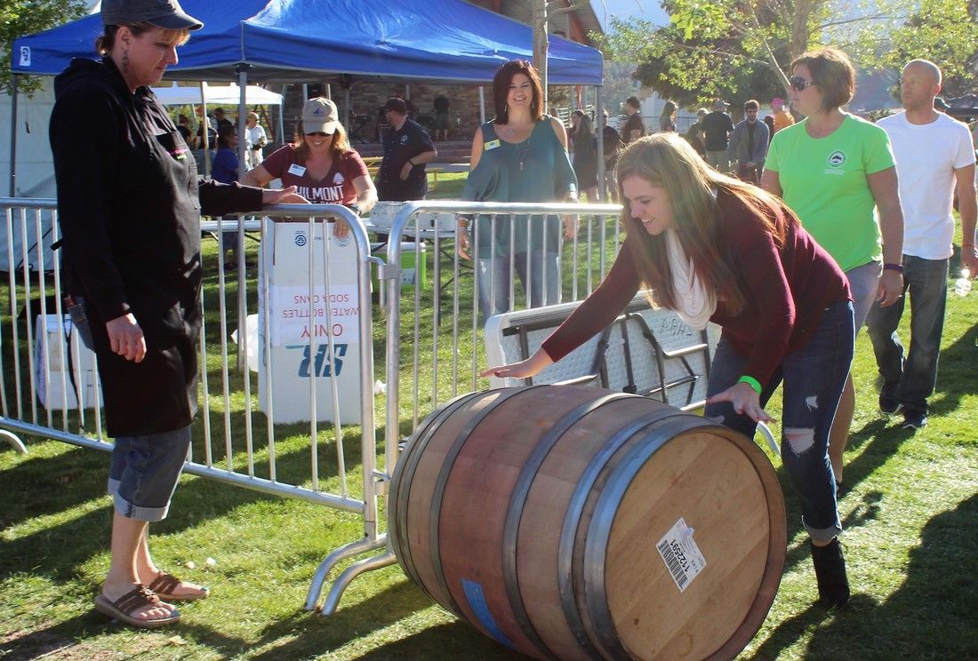 People at an outdoor event, interacting with a large barrel behind a metal barrier.