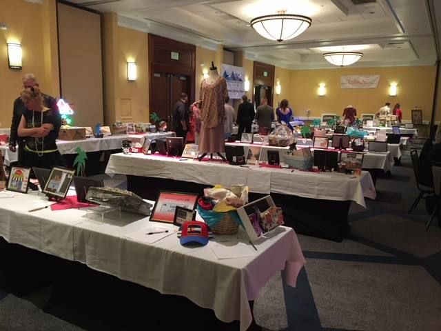 Room filled with tables covered in items for an auction; people browse and bid.