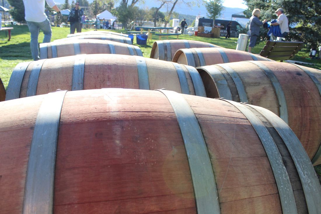 Row of wooden wine barrels, outdoor setting. People in background.