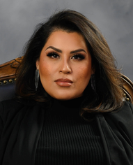 Woman with dark hair, wearing black blazer and top, looking forward.