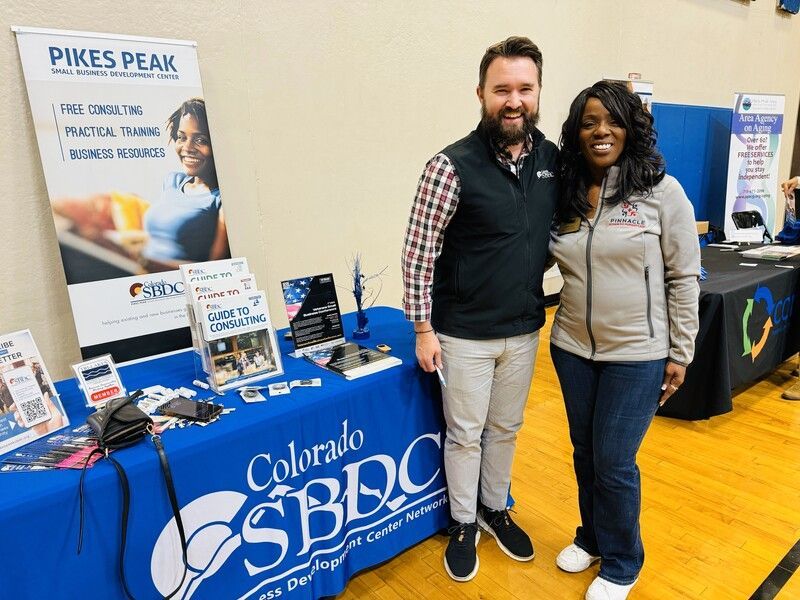 Two people at a Colorado SBDC booth; man with beard, woman smiling.
