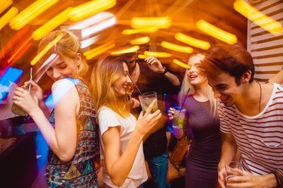 People dancing and drinking cocktails in a brightly lit nightclub.