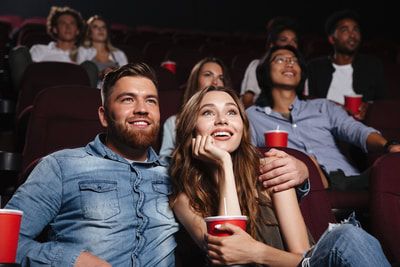 People smiling and watching a movie in a theater, holding drinks, and enjoying each other's company.