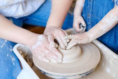 Hands of an adult and child shaping wet clay on a pottery wheel.