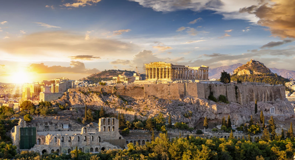 Acropolis of Athens at sunset, golden light illuminates the ancient structures against a blue sky.