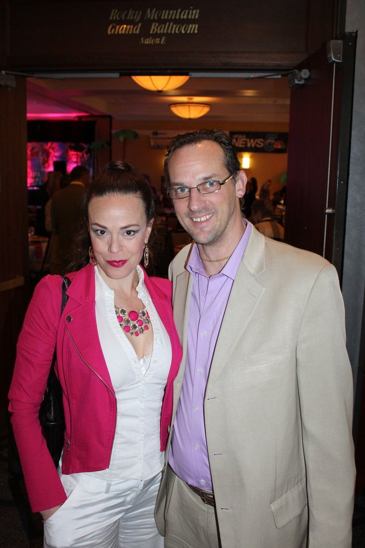 Woman in pink jacket and man in beige blazer pose together indoors.