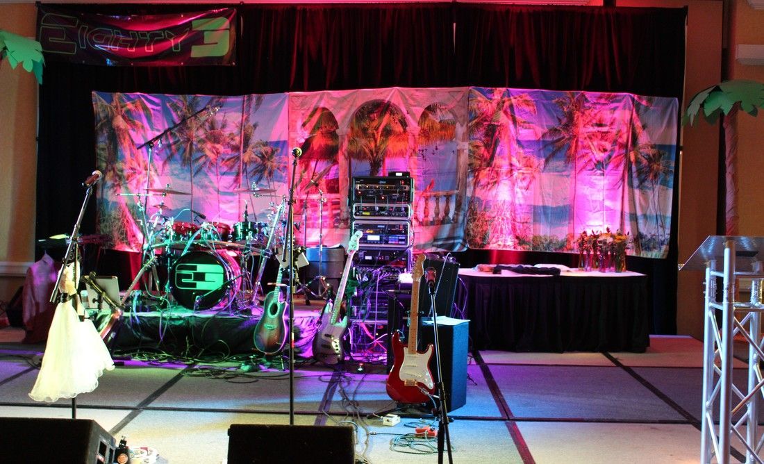 Band's stage set-up with drums, guitars, and sound equipment; colorful backdrop and lighting.