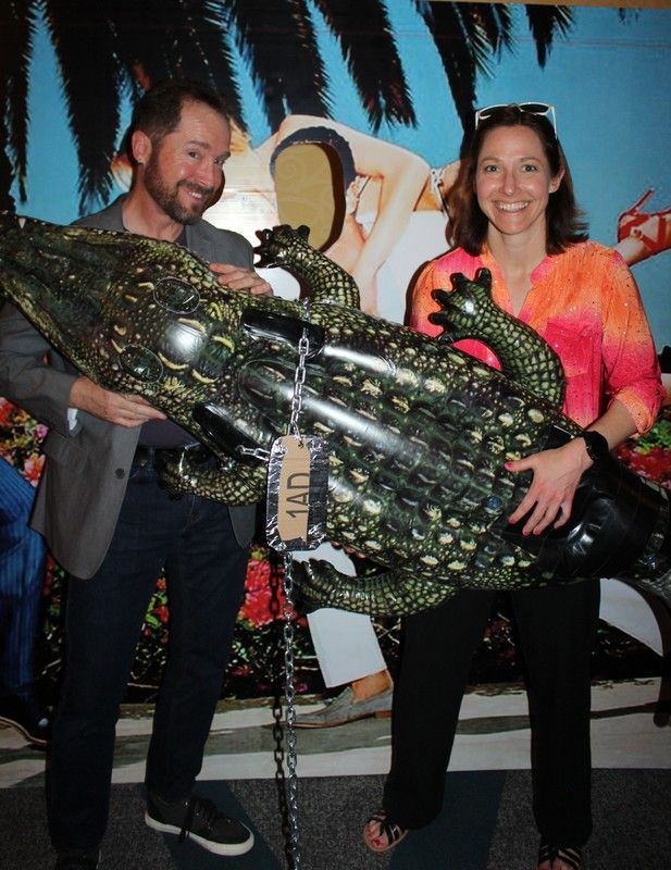 Man and woman holding a large inflatable crocodile in front of a colorful background.