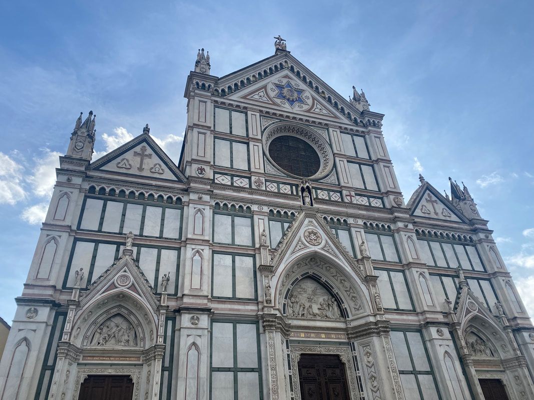 Exterior view of the Basilica di Santa Croce, Florence, Italy. White and grey facade, ornate architecture under a blue sky.
