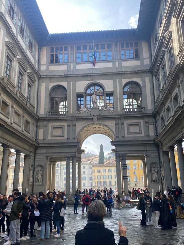 Courtyard view of Uffizi Gallery in Florence, Italy, with tourists and arched doorway framing a cityscape.