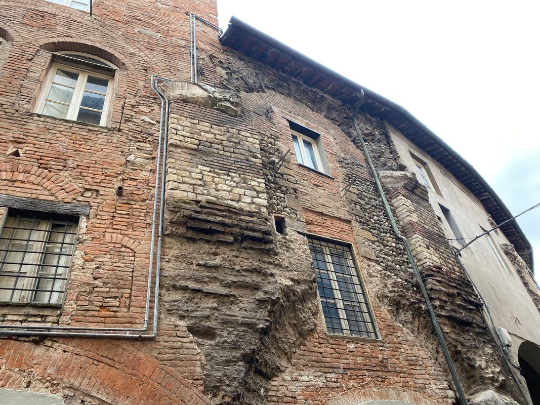 Red brick building facade with arched windows, metal pipes, and visible structural damage.