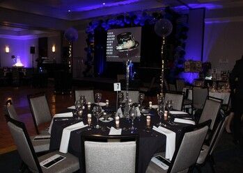 Round table set for a formal event with black tablecloth, chairs, and blue lighting in a large room.