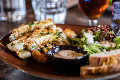 Grilled chicken with salad and dipping sauce on a brown plate, drinks in background.