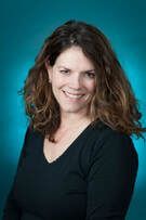 Woman with brown hair smiling, wearing a black shirt against a teal background.