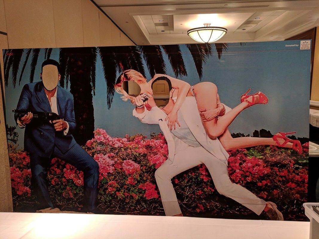 Photo booth with face cutouts: Man holding gun, man carrying woman through a flower field.