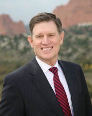Man in suit and tie smiles in front of a red rock mountain backdrop.