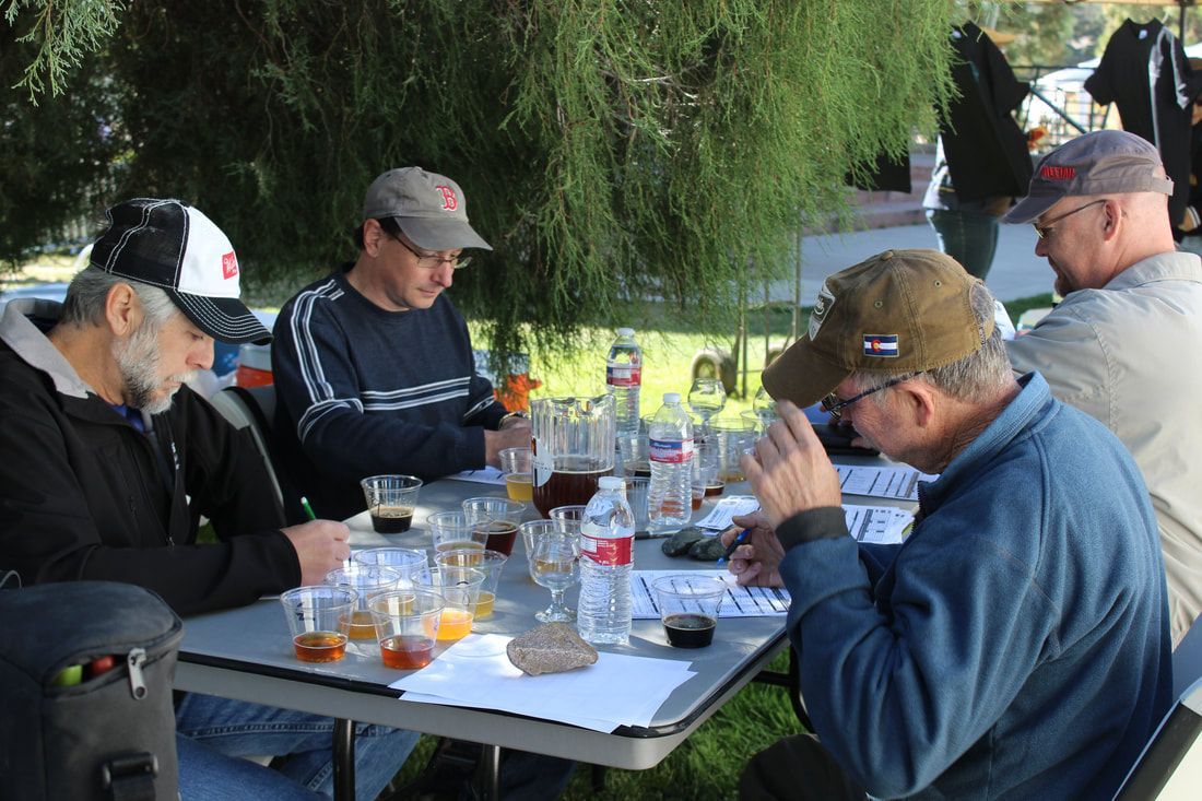 Four men in caps sample beers outdoors, taking notes.