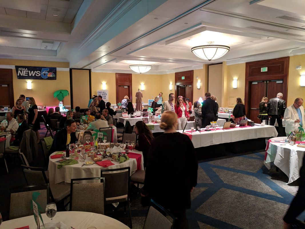 People at an event in a large room with tables and decorations, possibly a charity auction or gala.
