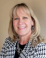 Blonde woman with a patterned jacket, smiling.