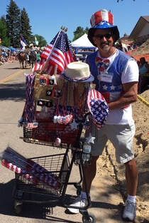 Man in patriotic attire with a decorated shopping cart full of American flags at an outdoor event.