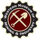 Logo for Western Museum of Mining & Industry: Cross pickaxe and shovel in a circular emblem with text.