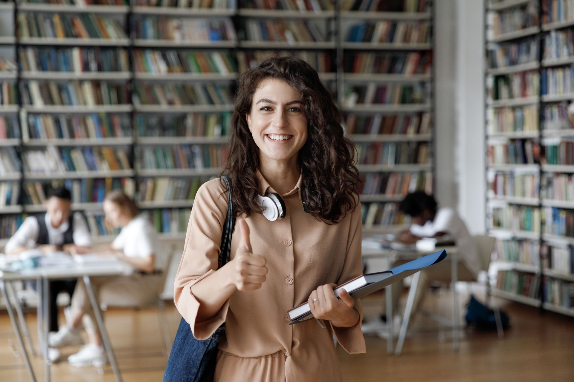 A woman is holding a folder and giving a thumbs up in a library.