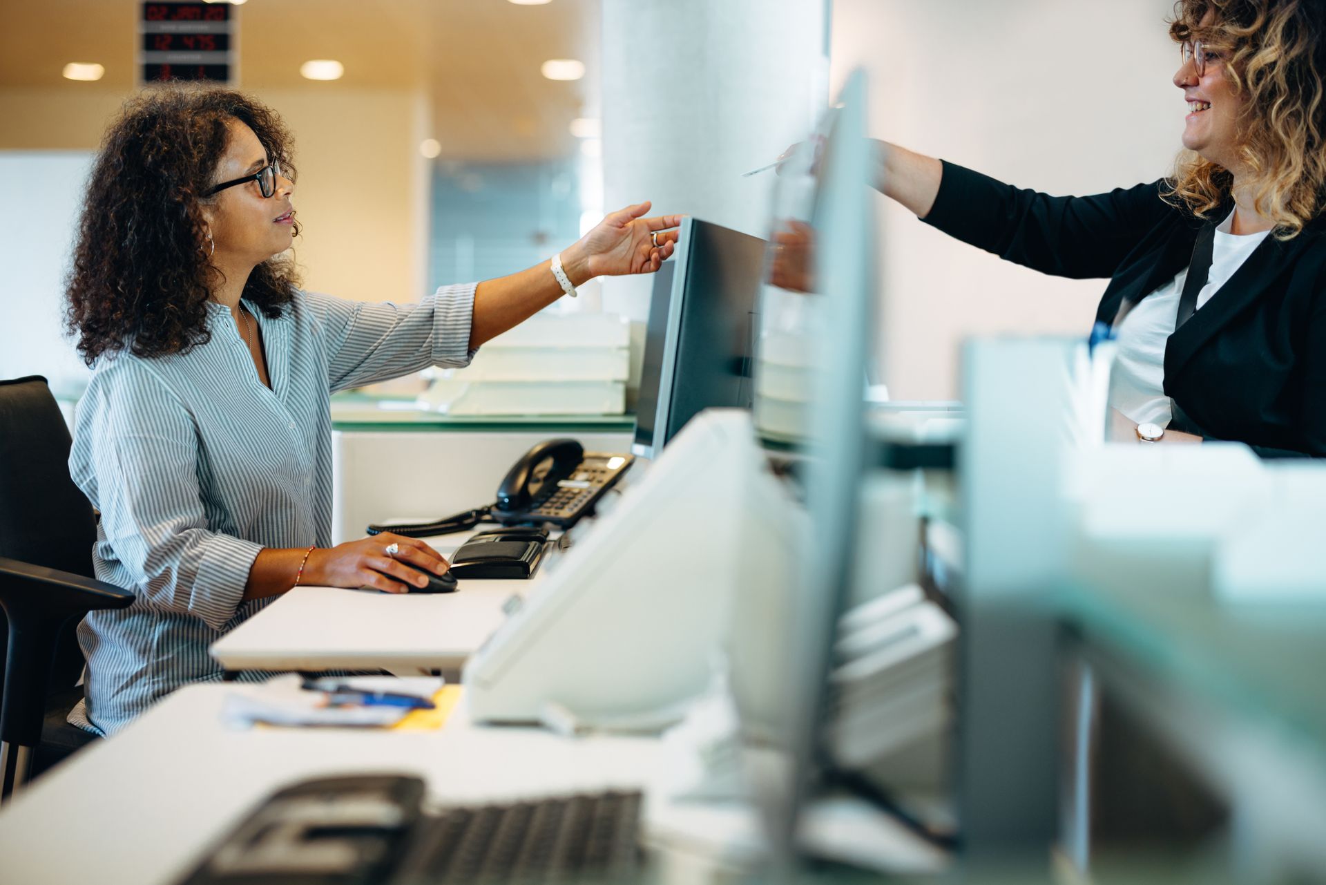Two women are sitting at a desk in front of a computer.