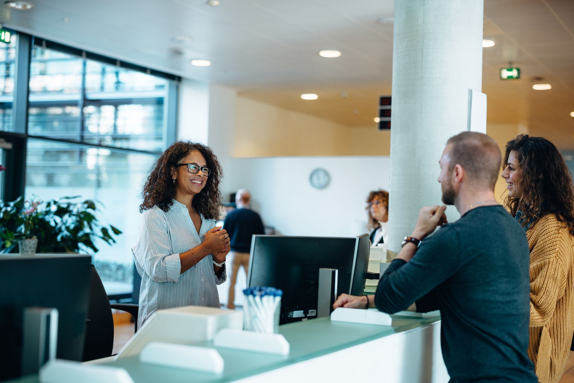 A man and a woman are talking to each other at a reception desk in a hospital.