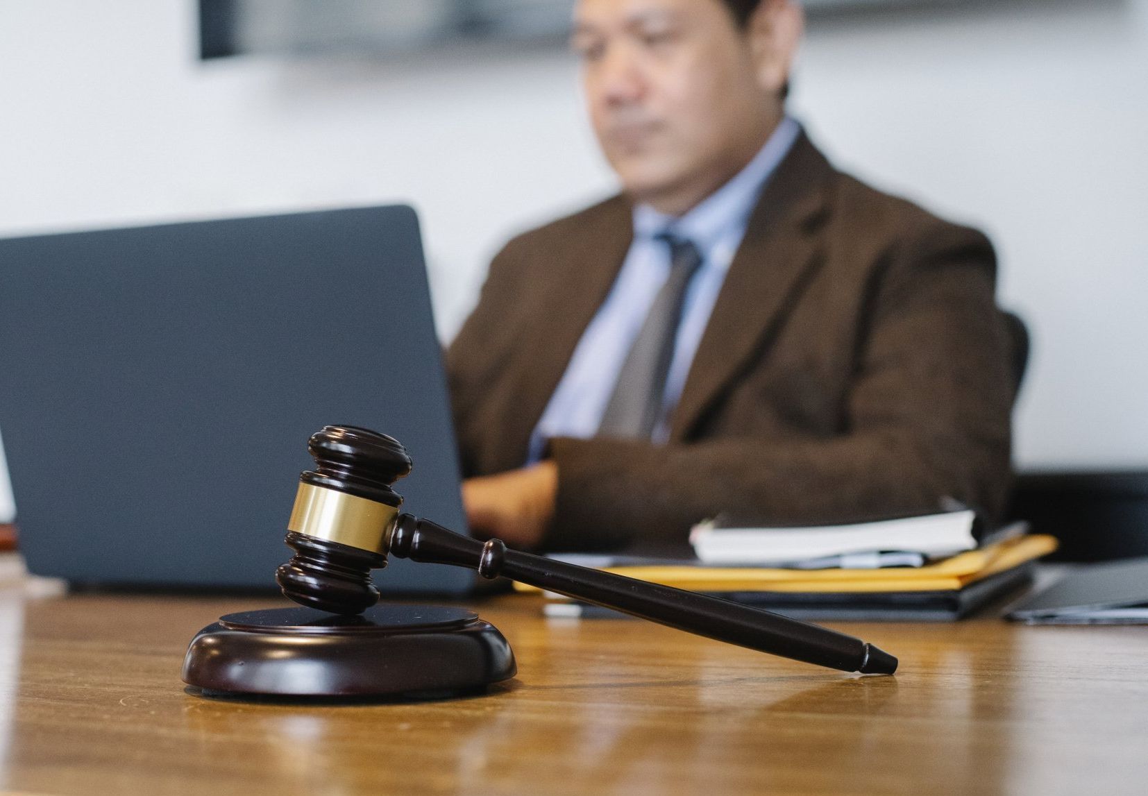 A man typing on a laptop on a desk with a gavel.