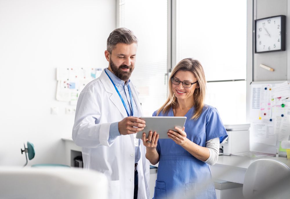 A doctor and a nurse are looking at a tablet in a hospital room.