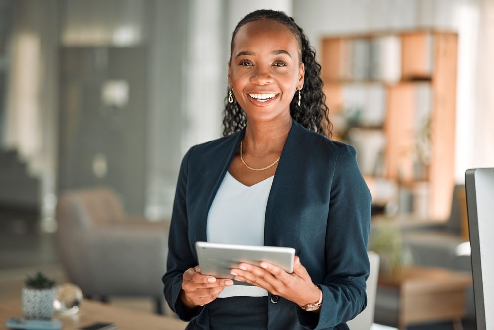 A woman in a suit is holding a tablet in her hands and smiling.