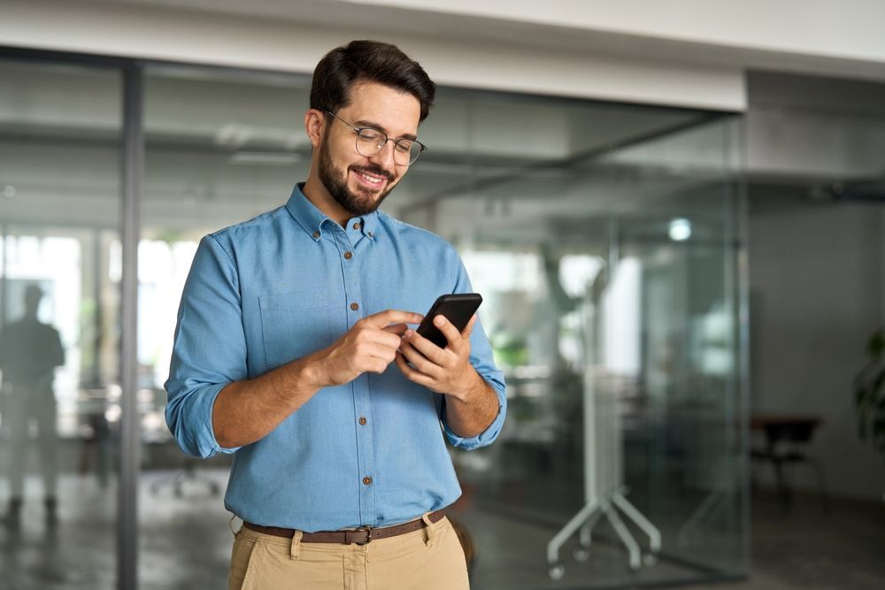 A man is standing in an office looking at his cell phone.