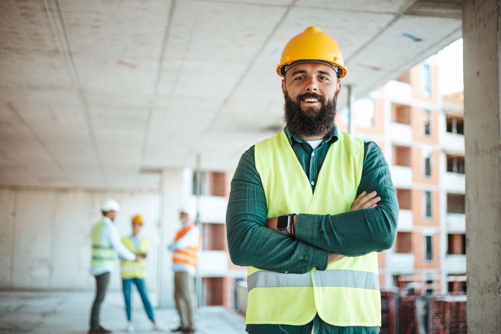 A construction worker is standing with his arms crossed at a construction site.