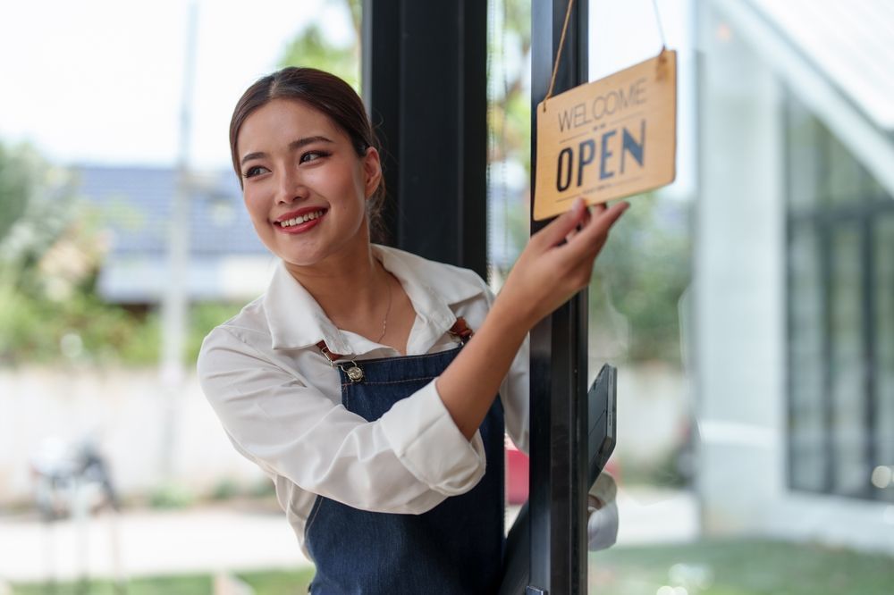 A woman is hanging an open sign on a window.