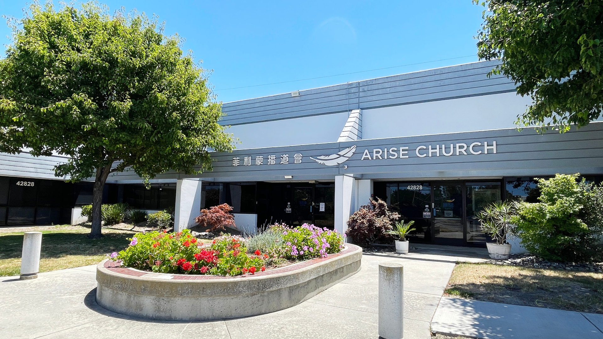 A church with flowers in front of it on a sunny day.