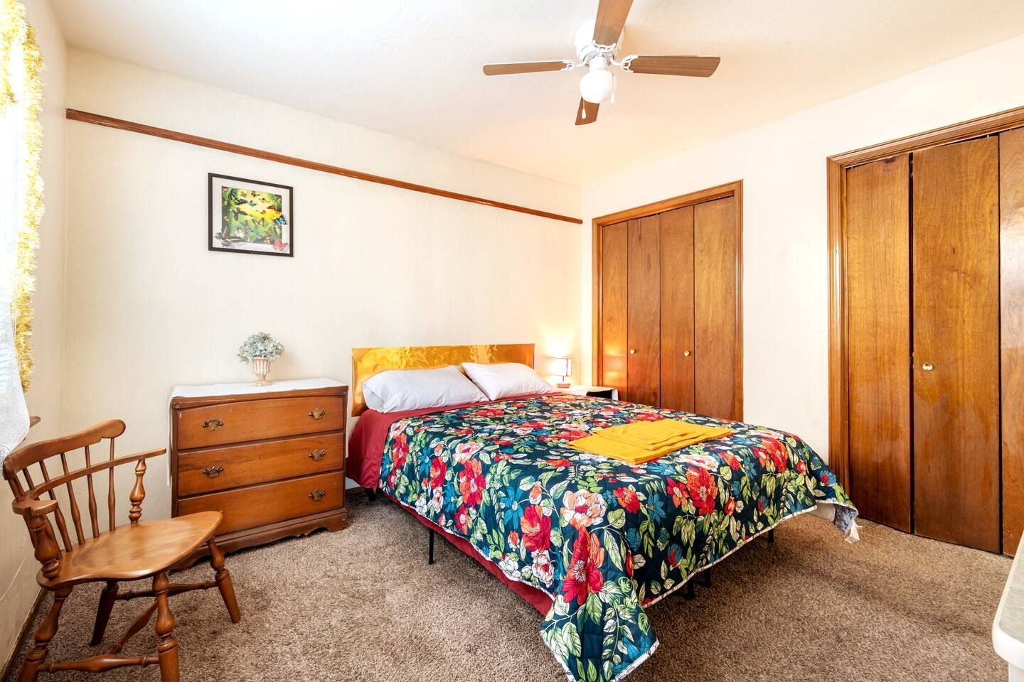 A bedroom with a bed , dresser , chair and ceiling fan.