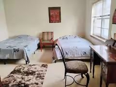 A bedroom with two beds , a desk , chairs and a window.