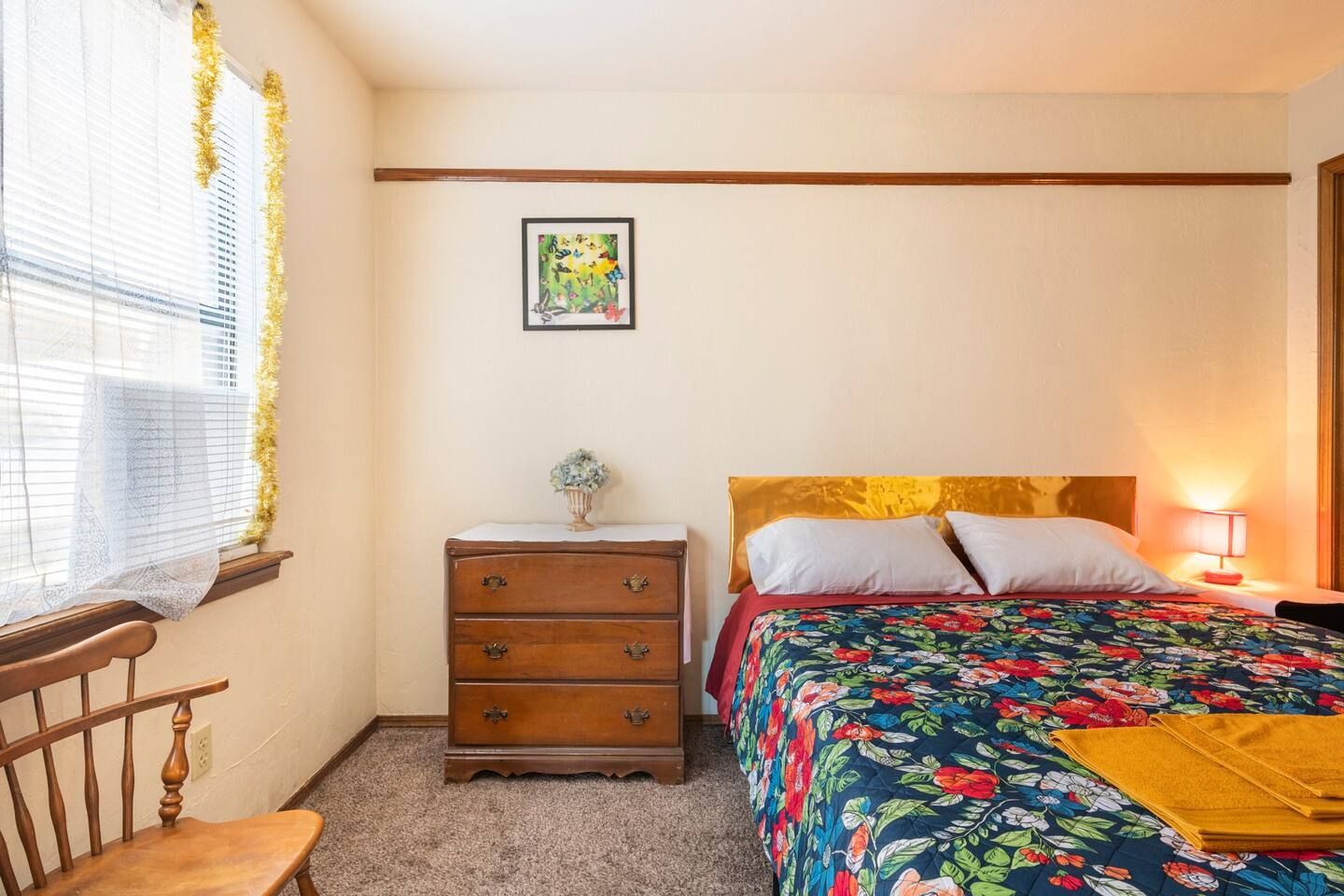 A bedroom with a bed , dresser , chair and window.