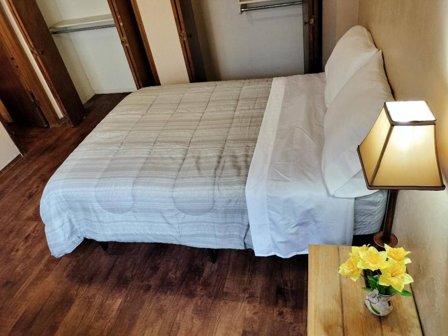 A bedroom with a bed a lamp and a vase of yellow flowers