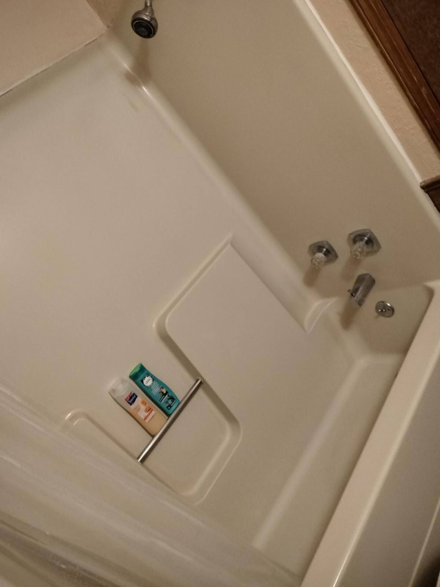 A white bathtub with a shower head and soaps on the shelf