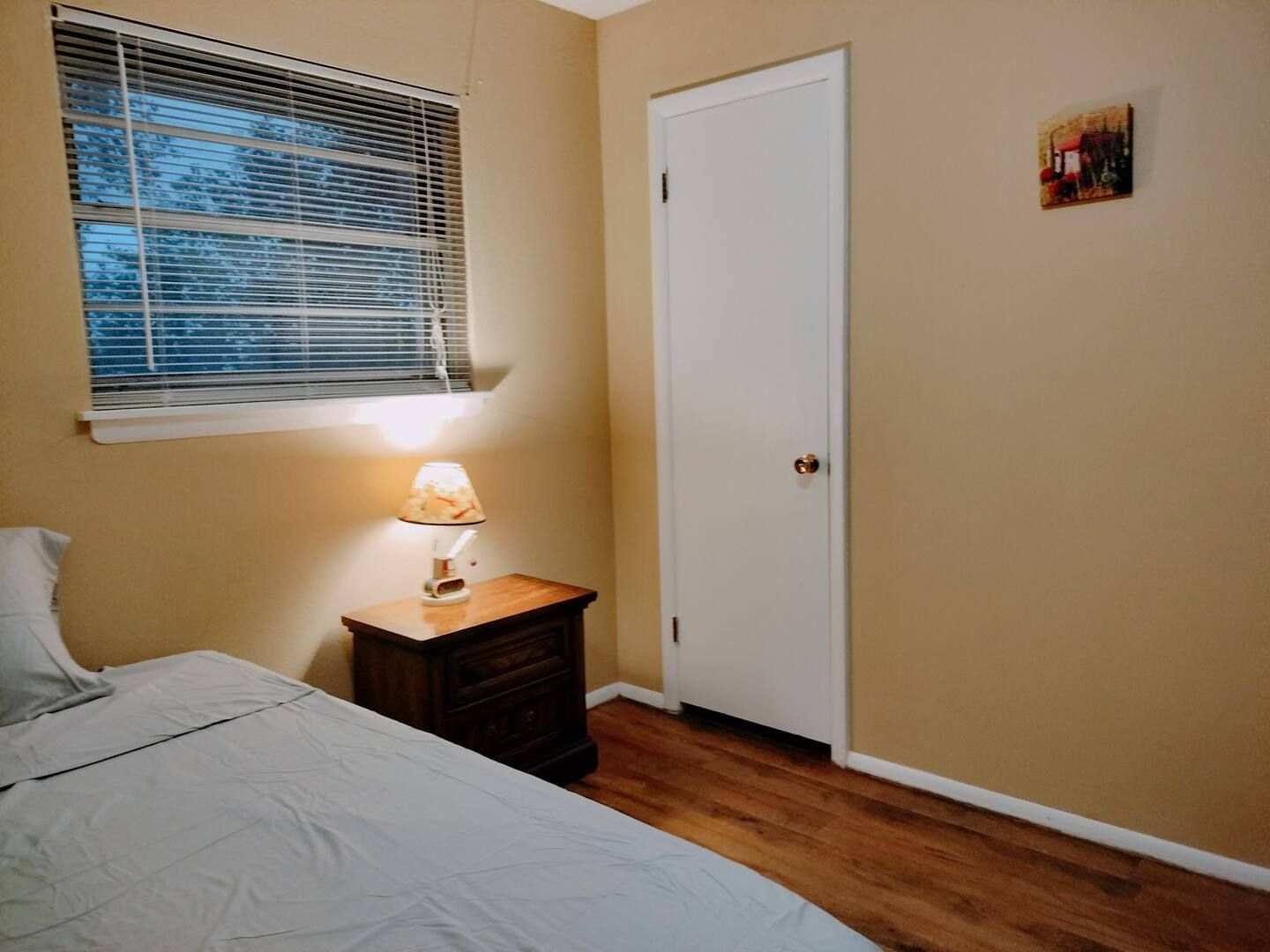 A bedroom with a bed , nightstand , lamp and window