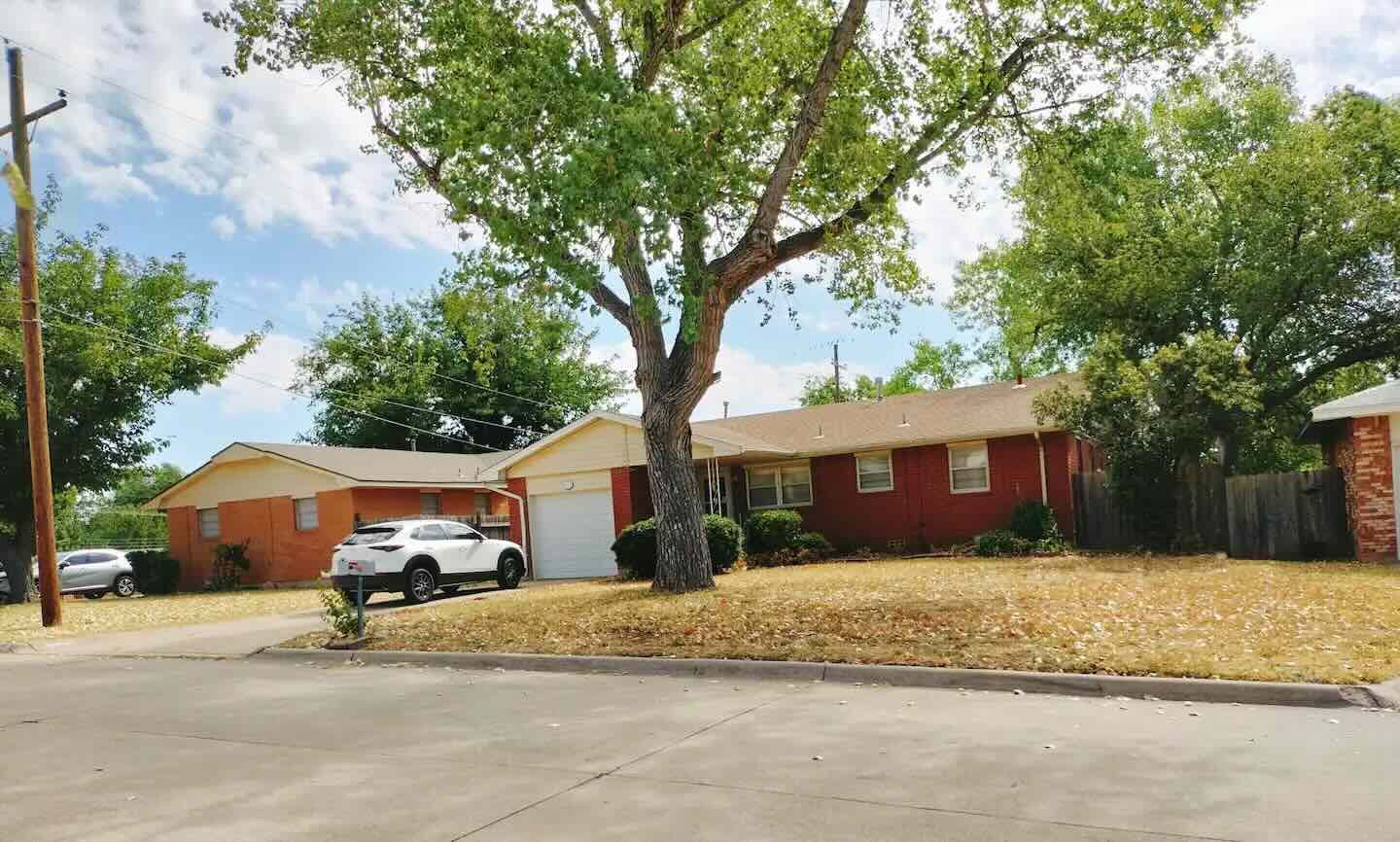 A white suv is parked in front of a red house.