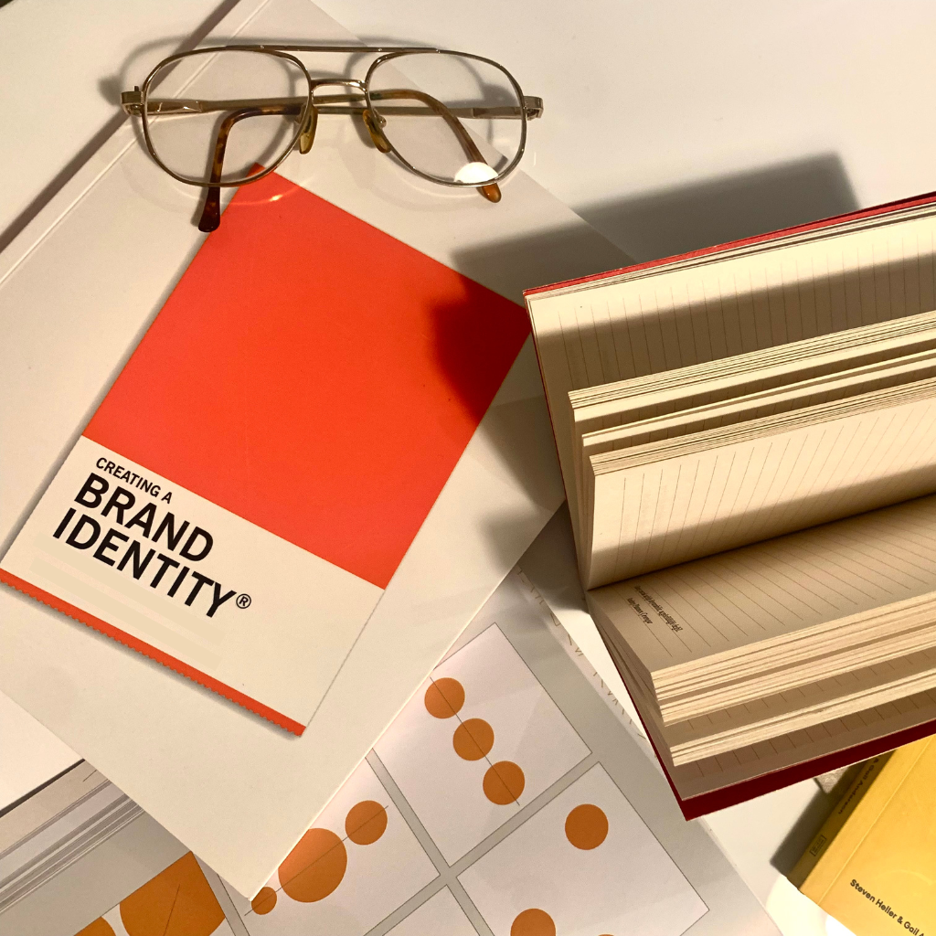 Glasses rest atop open books and documents related to brand identity.