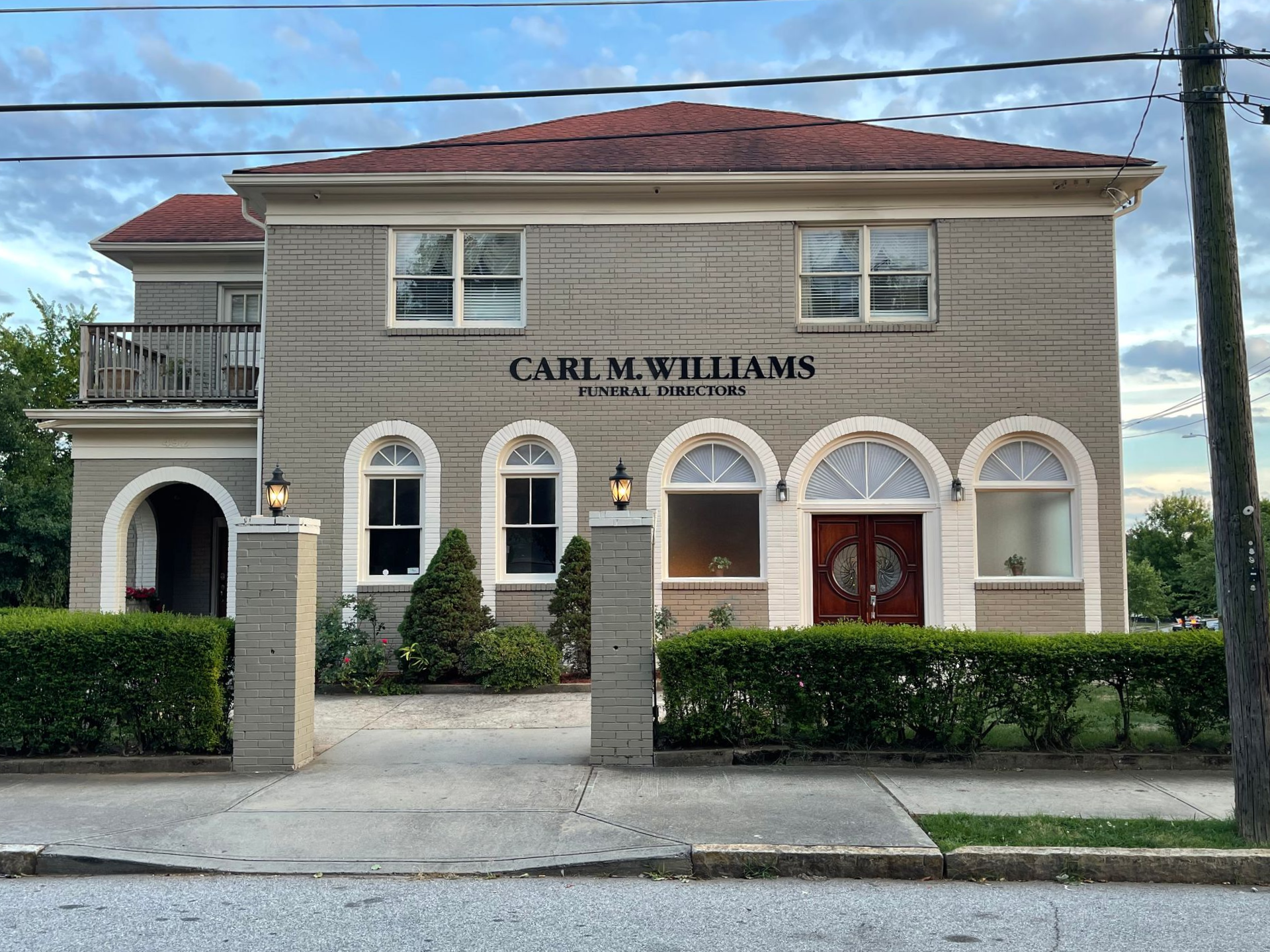 Gray two-story building with red roof, arched windows, and sign: Carl M. Williams Funeral Home.